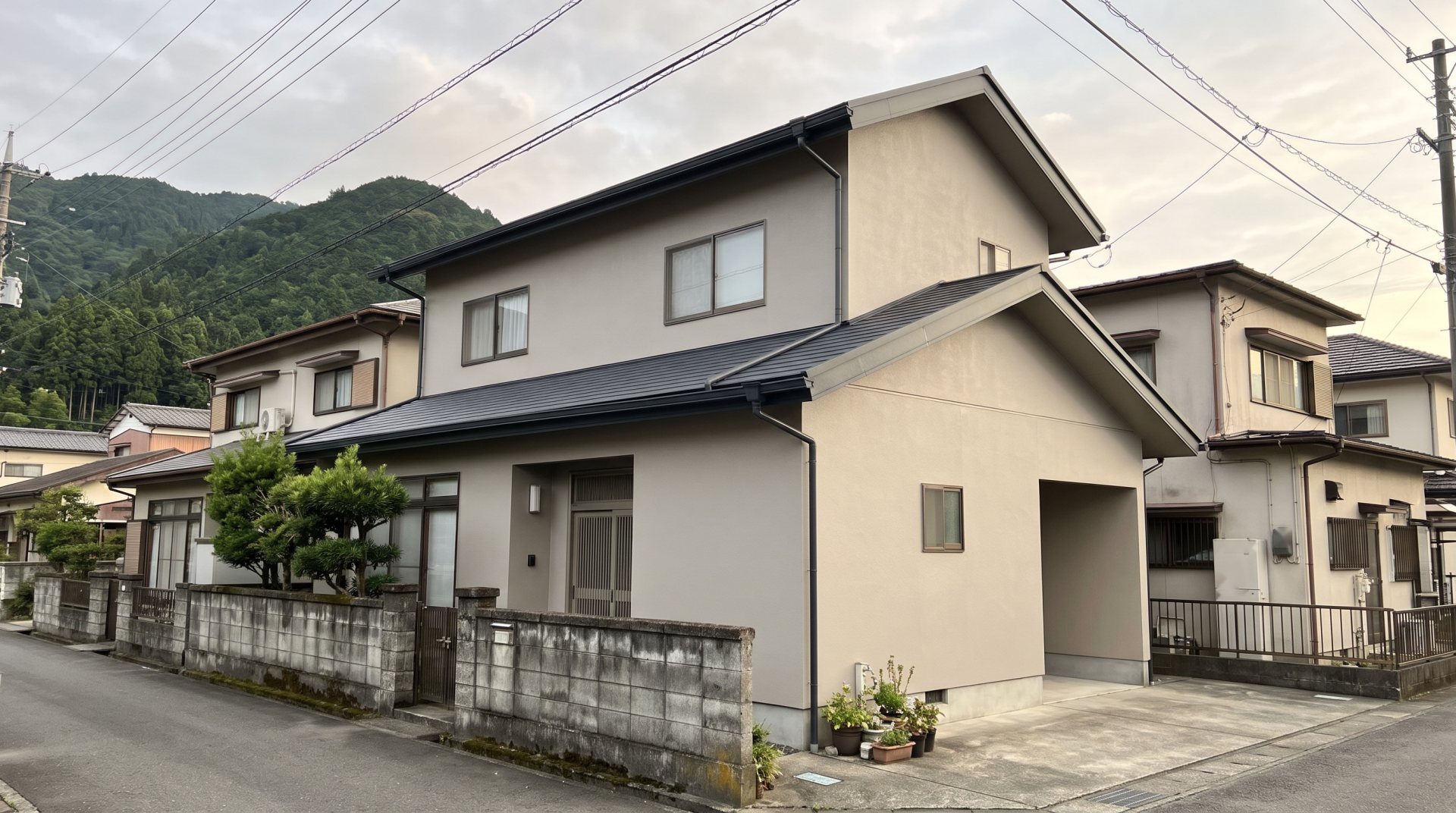 山の緑が近い住宅地で、外壁と屋根の塗り替えを終えた2階建ての家（イメージ）